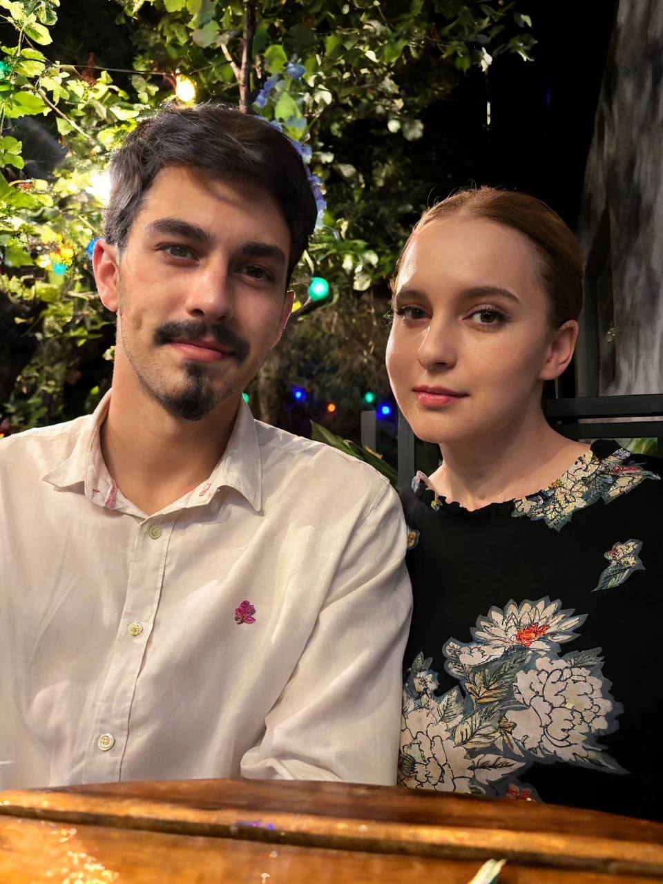 A beautiful woman and man with dark hair, dark brown eyes, and bright eyes, standing in a lush garden on a sunny day, surrounded by colorful flowers, with a cute expression and slightly split lips, blushing, in renesanse clothes 