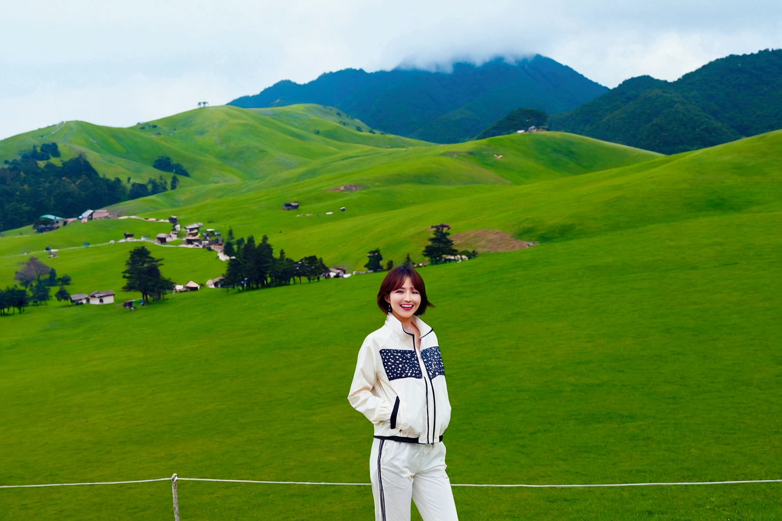 high quality, 1 woman, ((36 years old 건강한 한국 여성)), ((36 years old)), 1 woman, The eyes are big and beautiful. ((slim)), ((short medium hair)), laugh. pose: standing, High-end luxury brand windbreaker jacket, white casual pants, background: 1 woman, California, pasture, cattle, grass. With a 16-35 wide angle lens , look up to the side, cattle가 풀을 뜯는다,