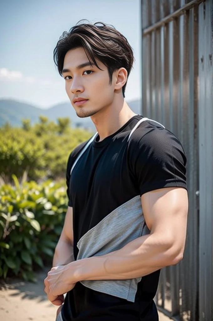 A young Asian man stands, handsome, muscular, looking at the camera. In a simple black t-shirt, Fieldside, grass, beach, sunlight