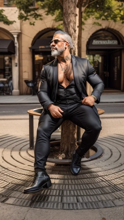 Image is a street-style photograph featuring a big huge beefy muscular morphed mature old muscle man sitting on a circular bench surrounding a tree. The man has a light skin tone, a well-groomed white beard, and is wearing dark sunglasses. He is dressed in a tight black blazer over a partially unbuttoned tight black shirt, skin tight black pants, and black boots. He has visible tattoos on his neck and chest. The background shows an urban setting with arched doorways in the distance. The overall color palette is muted, with a focus on the man's stylish attire and confident pose