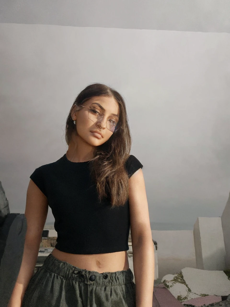 documentary photography of of kyliejenner, black hair, eyes shadow ,rim lighting, on a coast, sharp focus, Windy , Long coat,