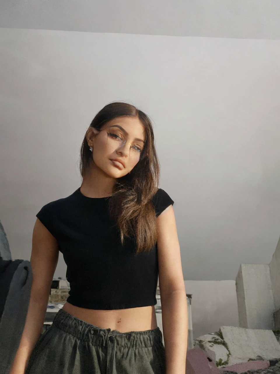 documentary photography of of kyliejenner, black hair, eyes shadow ,rim lighting, on a coast, sharp focus, Windy , Long coat,