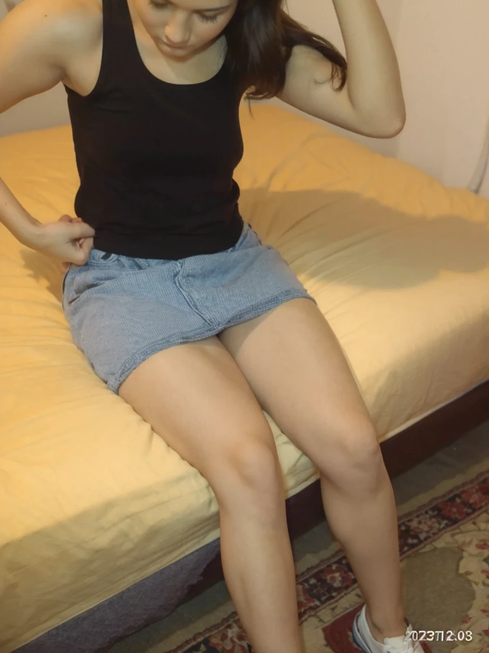 Woman wearing a thong sitting on the bed with her legs crossed with nothing on her looks at her phone