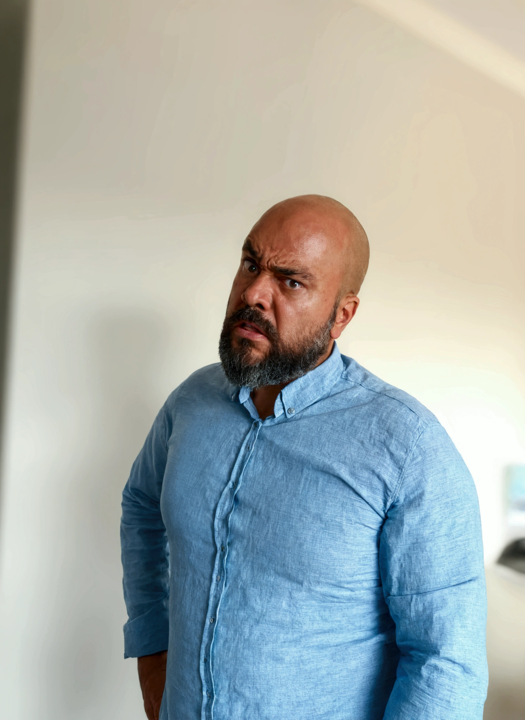 There's a man with a beard standing in a room, with serious facial expression, serious and severe expression, angry looking at camera, Looking away from the camera, serious and focused look, An expression of anger, looking furious, looking to the side of the camera, angry look in his face, photo of a man, Looking away from the camera, looking confused, looking angry