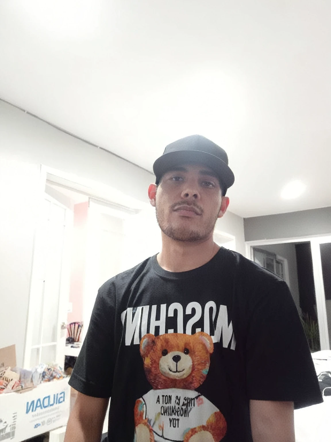 hay un hombre parado en una habItacIón con una camIsa negra y un sombrero, with a rap cap on his head, él lleva una camIseta negra, carmelo blandIno, Imagen de muy muy baja calIdad, I, 8k selfie photography, he is wearing a hat, frontal photo