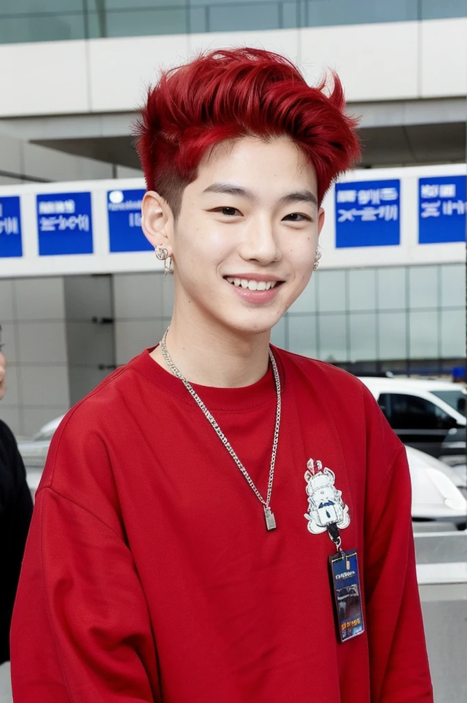 A Korean-Thai boy stands at the airport, smiles at the camera. He has red dyed hair and wears a hip-hop outfit. He also has an earring. Paparazzi take pictures of him. 