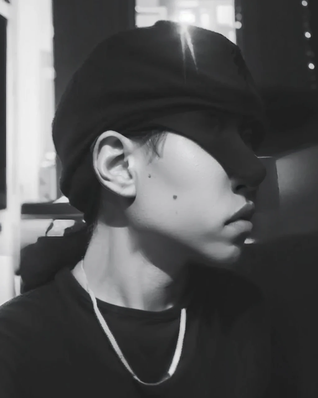 realistic black and white image of a boy wearing a cap, sitting and wearing a hoodie. His expression should be serene and thoughtful, with attention to the details of the sweatshirt and cap textures."
