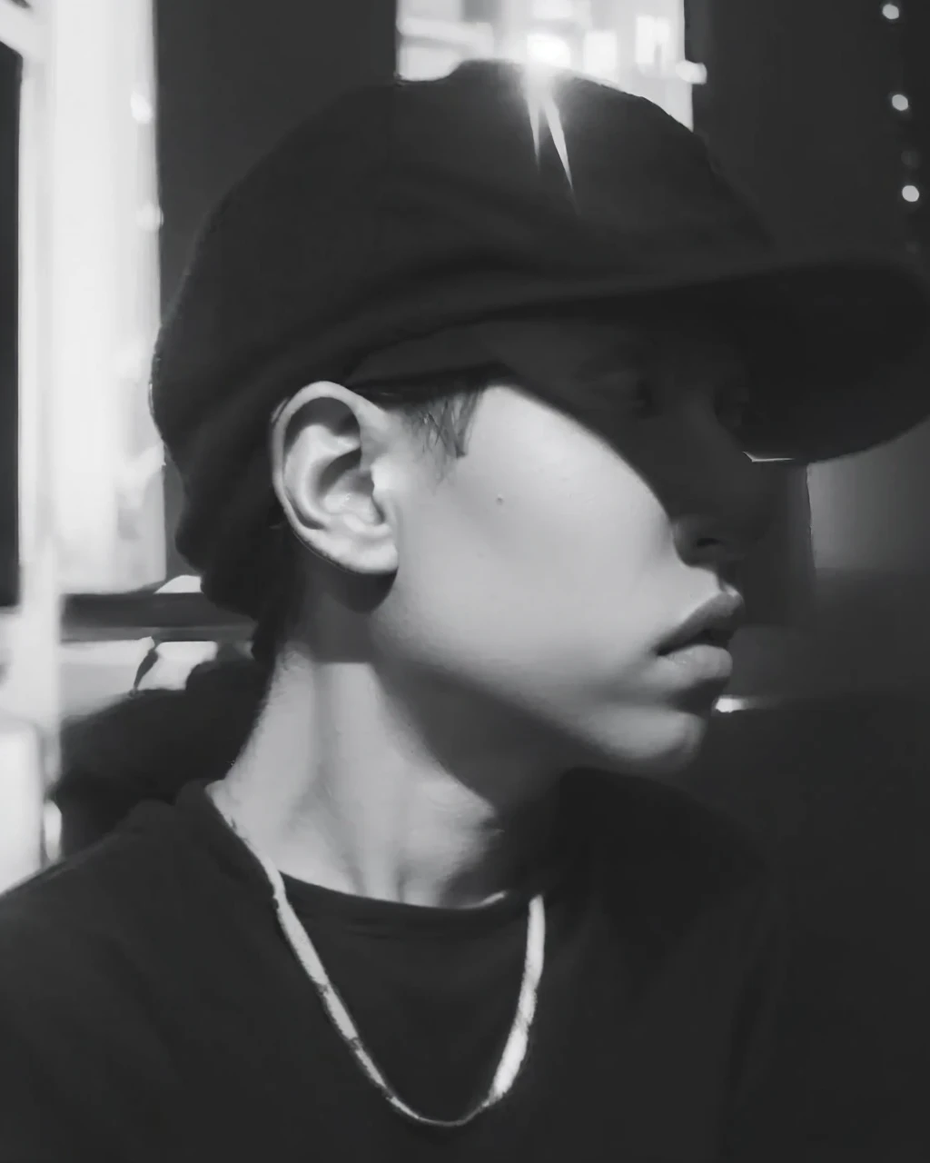realistic black and white image of a boy wearing a cap, sitting and wearing a hoodie. His expression should be serene and thoughtful, with attention to the details of the sweatshirt and cap textures."