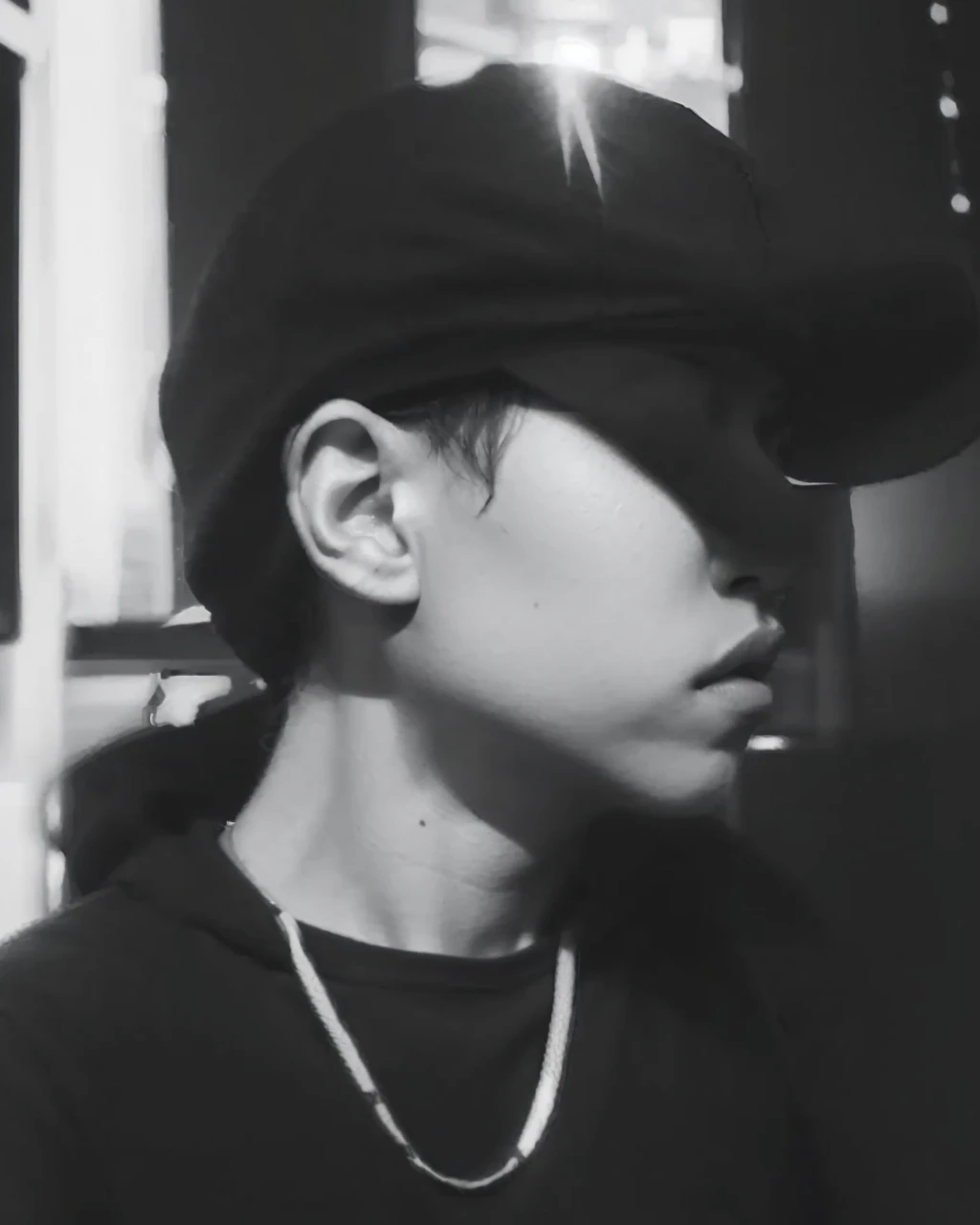 realistic black and white image of a boy wearing a cap, sitting and wearing a hoodie. His expression should be serene and thoughtful, with attention to the details of the sweatshirt and cap textures."