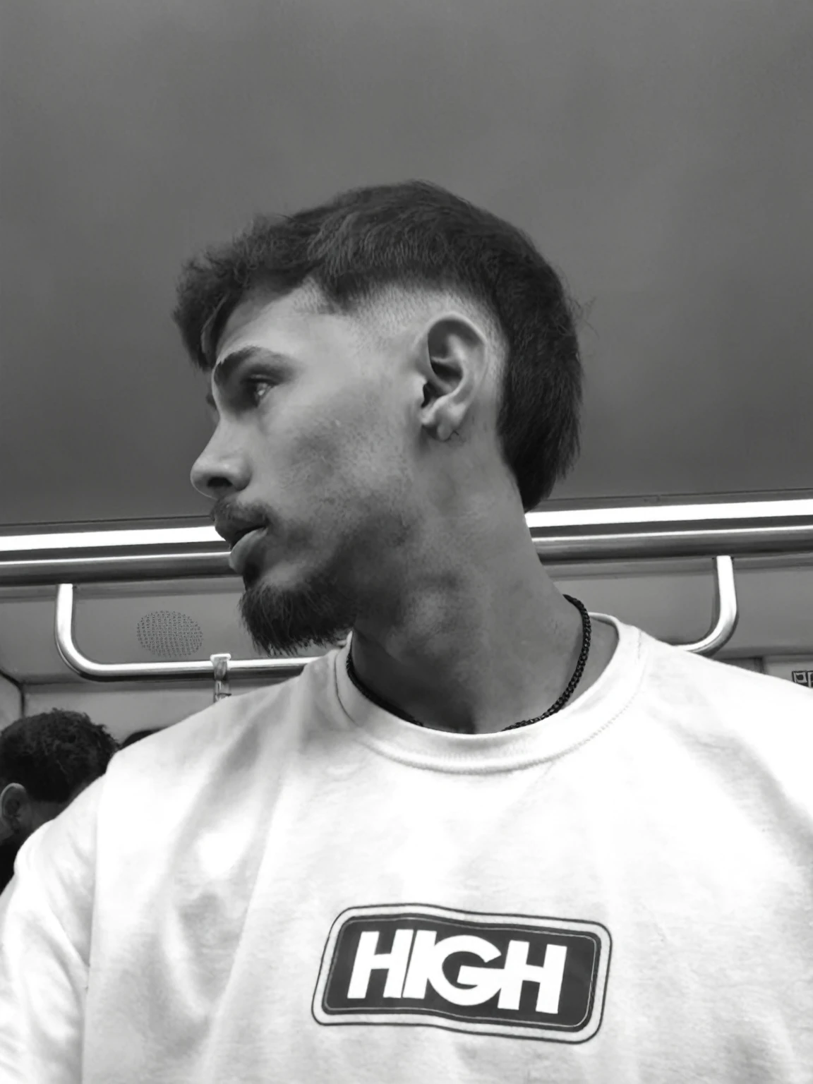 trimmed man in a white shirt on a subway train, cropped haircut, short on sides, short goatee, short hair on top of the head, cropped hairstyle, centralized portrait not side profile, modern haircut, half shaved haircut, looking to the side of the camera, cabelo short on sides da cabeça, centralized side profile portrait, fashionable haircut