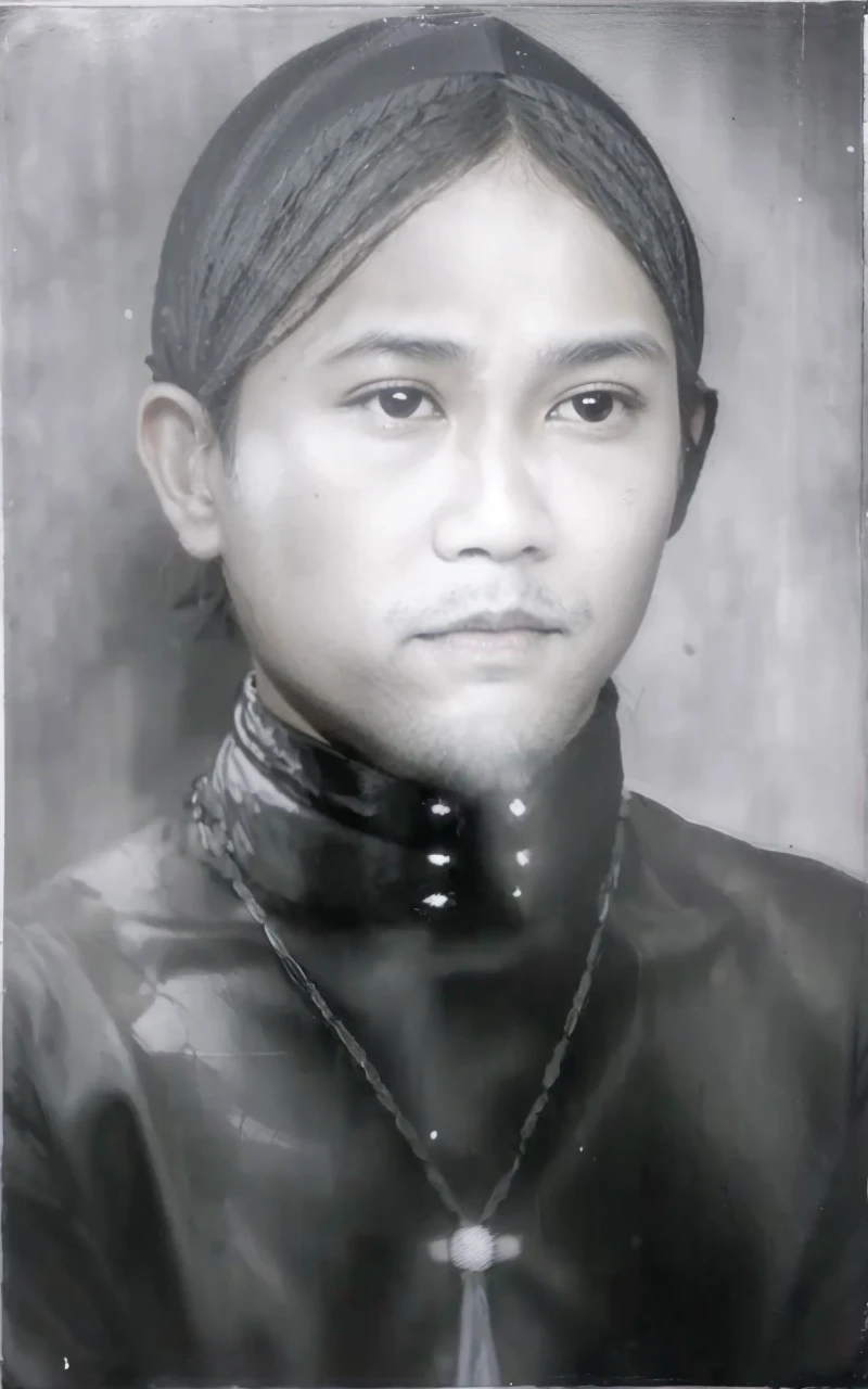 Indonesian Muslim man, 45 years old, brown skin with wrinkles according to age. small, closed lips, long natural black eyebrows, clean shining black eyes. flat nose. oval face, long chin. thin mustache and beard. wearing a black head covering, perhaps a type of blangkon, and kanigaran type clothes with the nuances of a prince. You can see a necklace hanging around the neck with a long, horizontal jewel-like fruit with a realistic HD quality image.
