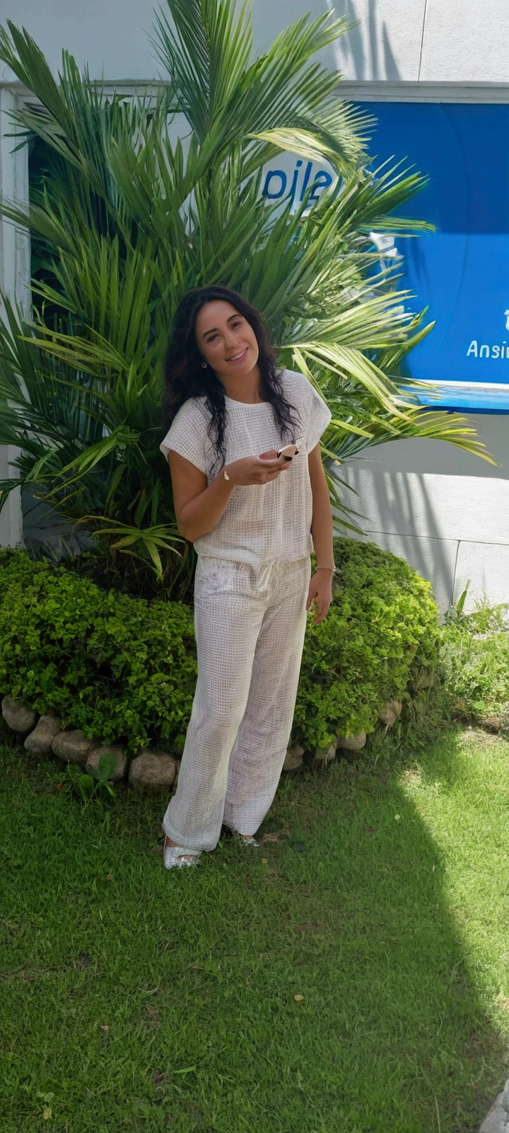 There is a woman standing in front of a building with a cell phone., in white clothes, wearing white pajamas, White suit, Wearing white clothes, worn - white style, all white, 30 year old Cuban woman., with a great pose, in front of a white background, Full body photo, Satisfied pose, Alanis Guillén
