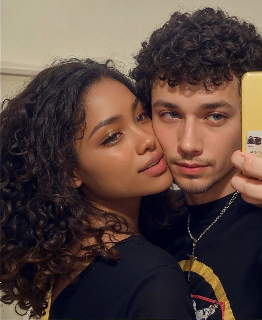 A white man with a goatee and eyes half-closed with a serious expression holding his cell phone looking at the camera and his girlfriend the black woman with her face pressed to his and smiling.