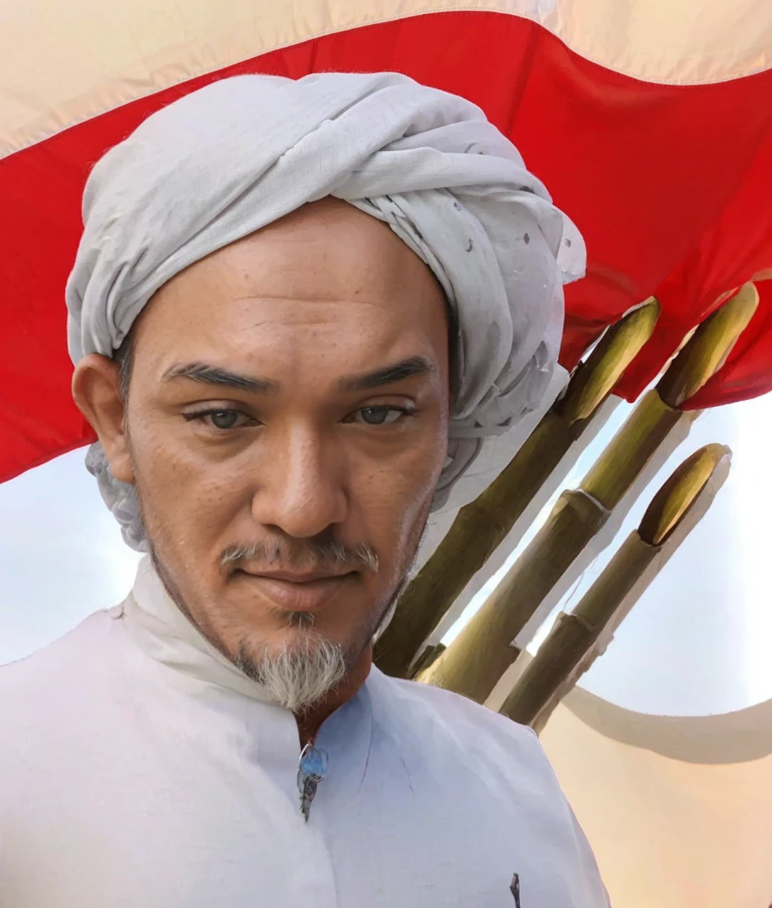 Indonesian Muslim man, 70 years old, wrinkled brown skin according to age. wearing a white patterned turban and Islamic clothes. clear black narrow eyes, thick gray eyebrows, thick mustache, long beard. big tall nose, big wide ears, oval face, naturally wrinkled forehead. mouth covered with thin lips. In the background of the Indonesian red and white flag, you can see three sharp bamboos on it. HD quality realistic images.