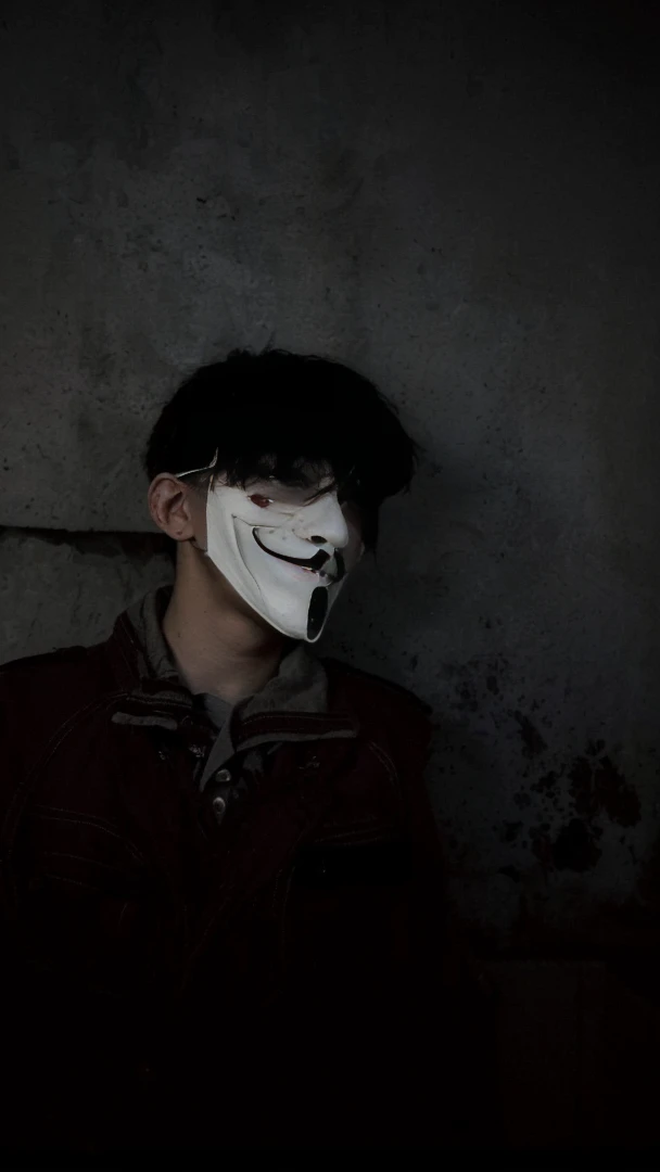 arafed man wearing a mask with a creepy face, twisted god with no face, darkwave goth aesthetic, anonymous mask, anonymous, masked person in corner, in an alleyway during the purge, creepy aesthetic, broken mask, pale white face, dark academia aesthetic, photo of scp-173, bladee from drain gang, scary look, horror aesthetic