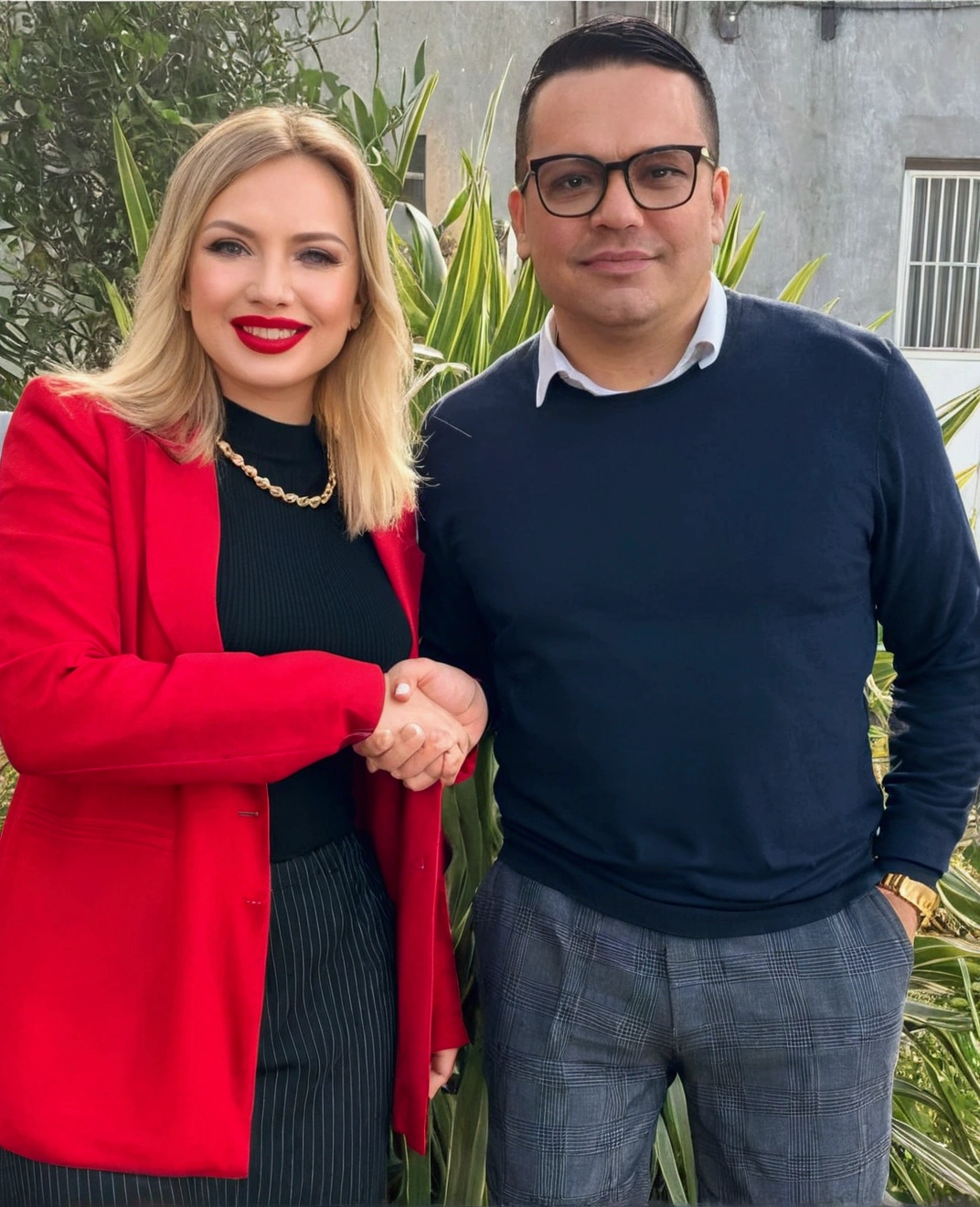 blonde woman in a red blouse without glasses with lipstick and a man with glasses with black hair in a black blouse without lipstick