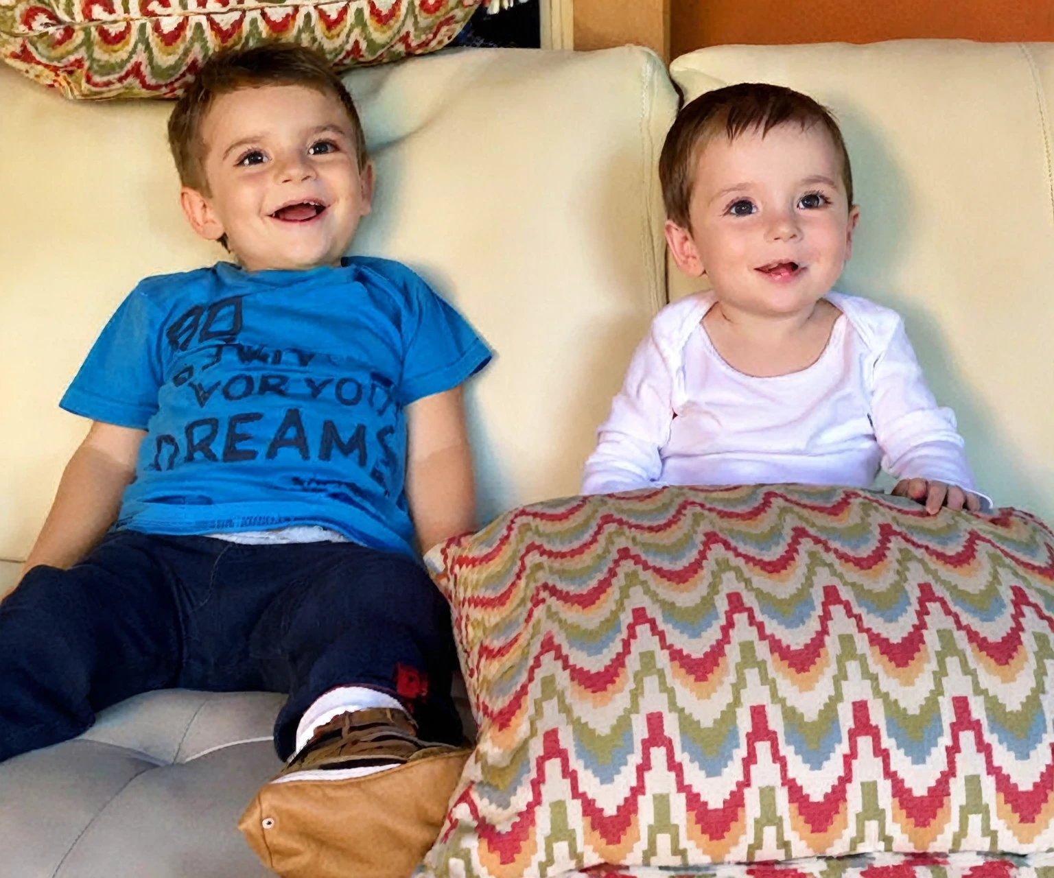 there is a boy and a woman sitting on a sofa with cushions, they are smiling, gorgeous faces, sweet appearance, They are close to each other