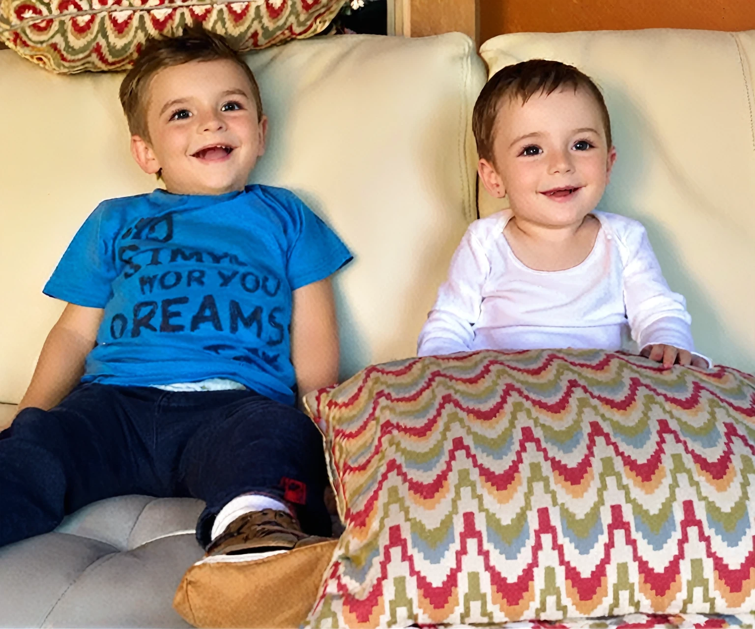 there is a boy and a woman sitting on a sofa with cushions, they are smiling, gorgeous faces, sweet appearance, They are close to each other. put them at with the same characteristics
