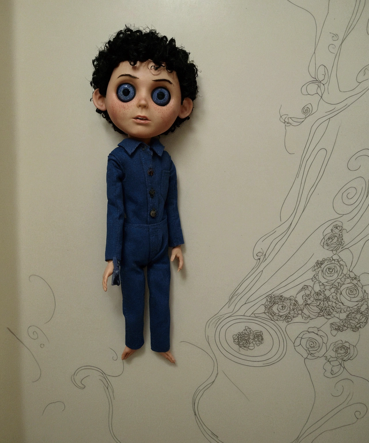 Man doll based on the Coraline movie. He's in a horror movie, there are several dead dolls on the floor. He has curly hair, short black curly. Your eyes are black. Caucasian skin