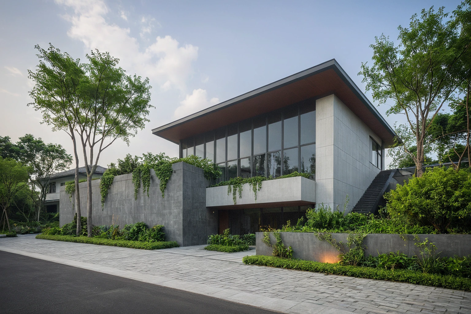 A modern villa situated on a street, basking in daylight. Surrounding the villa are lush tropical trees, green shrubs, and plants that add a vibrant touch of nature. The vivid colors of the vegetation create a striking contrast against the foggy and moody ambiance of the street. The villa boasts large glass windows and doors, constructed with high-quality, ultra-realistic glass that reflects the environment beautifully. The structure is made of solid concrete with a minimalist design, predominantly in dark grey tones. The interior glows with warm lighting, creating a welcoming atmosphere. The villa features modern materials and finishes of the best quality, resulting in a true masterpiece of contemporary architecture. The scene is enriched with streetscapes that blend seamlessly with the villa’s design, enhancing the overall aesthetic.
