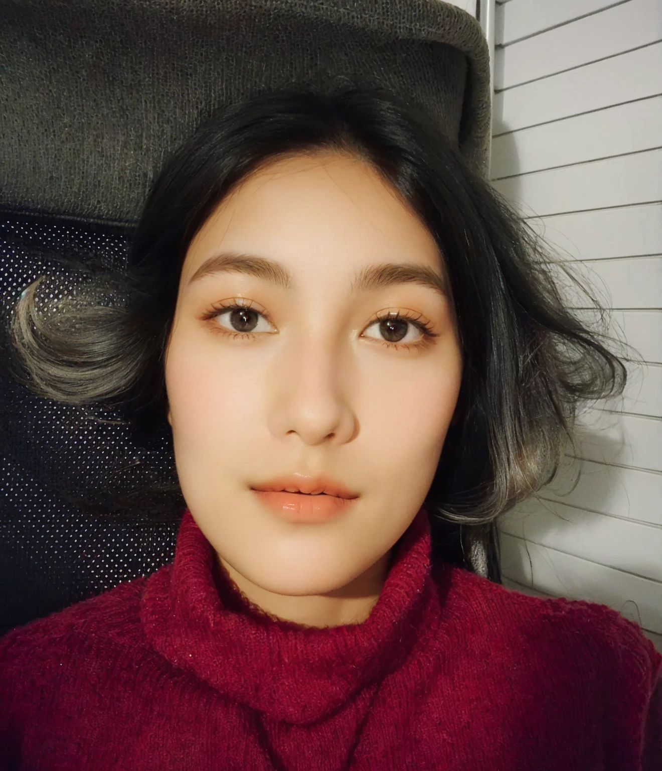 femme avec un pull rouge et une chaise noire, 18 ans, avec un visage précis, sans maquillage, peau bronzée, avec une expression de visage sérieuse, souriant, photo frontale, selfie d'une jeune femme, portrait de face, regardant directement la caméra