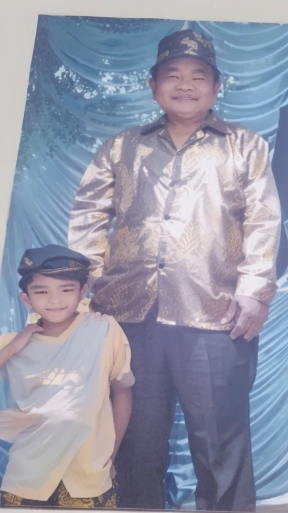 portrait of a middle-aged man wearing a golden batik shirt with a black cap, standing with a boy