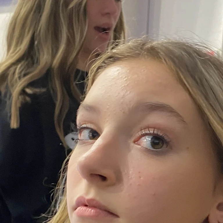 there is a girl that is sitting down with a cell phone, looking to the side off camera, looking defiantly at the camera, looking away from camera, looking away from the camera, taken in the early 2020s, very very low quality picture, she is facing the camera, looking straight to camera, detailed unblurred face, completely naked
