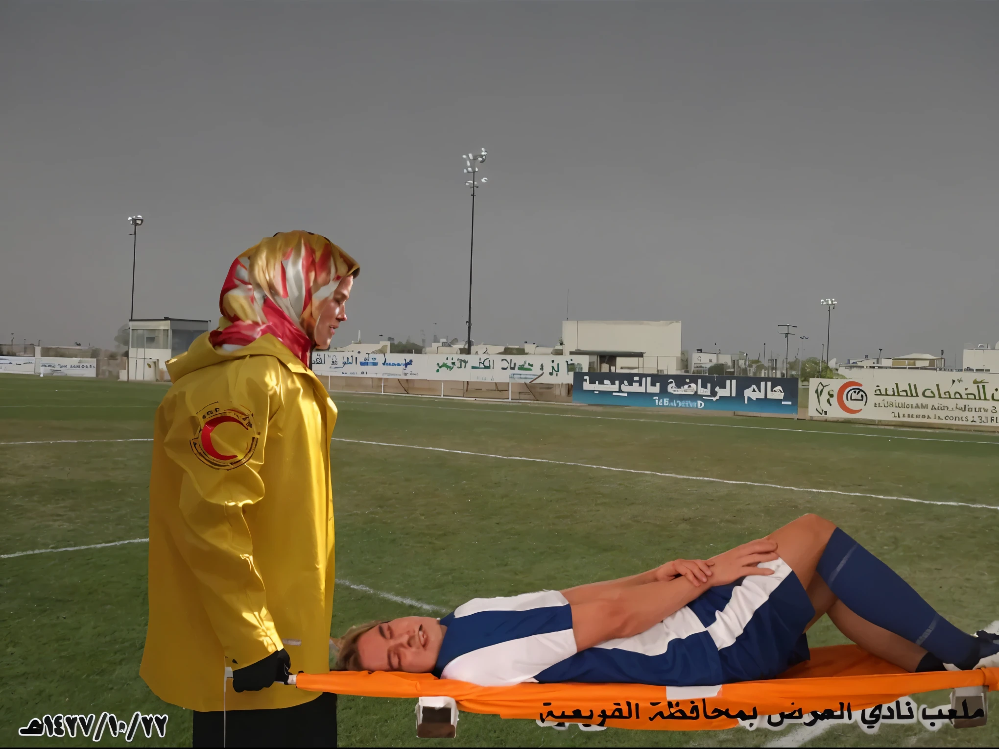 there is a male soccer player in short sportswear lying injured on a stretcher, there is an injured sportsman who is covering his face on a stretcher, an injured sportsman is covering his face with his hands, an injured sportsman is writhing ecstatic in pain on a stretcher, dramatic pity pose, there is a very female woman in a high-shine coat, a high-shine black wetlook coat, a long shiny coat, a wetlook glossy coat, a wet black laquered coat, a very female looking wife is wearing a wetlook coat, injured, medic, soccer action pose, affection pose, lecherous action pose, dramatic action pose, theatralic pose, there is an attractive woman that is carrying a suffering man on a stretcher, there is a beautiful woman in a shiny coat who is carrying a blond man on a wet orange stretcher, a longhaired beautiful woman in a high-shine coat, a longhaired woman in a shiny downcoat, a woman is carrying a stretcher with a shorthaired man who is wearing shorts and a t-shirt, a weak man in spots shorts is consciousless and needs to be carried on a wetlook pvc stretcher, a shorthaired man with closed eyes is carried on a stretcher by a longhaired woman, a woman looks very scared and terrified, a consciousless man with closed eyes is suffering very much and has a very painful face, photo, photo shoot, photographed , accident, help, aid, first aid, pityg a man on a stretcher inside a sports Stadion, Sportszene, Stadion
