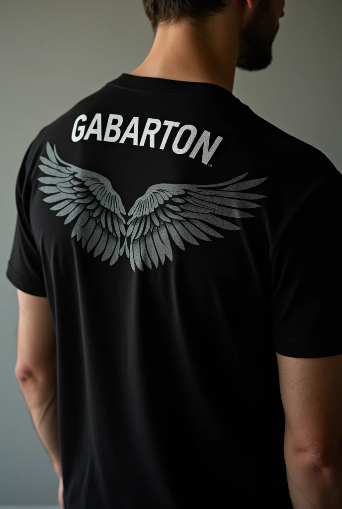 Photo of a plain black t-shirt called GABARTON on the back of his shoulder and there is a picture of wings 
