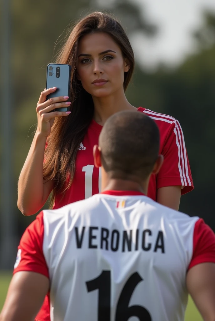 A very sexy woman with a soccer shirt in the upper middle part of the photo with a cell phone on her face taking a photo and in the lower middle part a man with his back turned with a soccer shirt and on the back it says VERONICA 