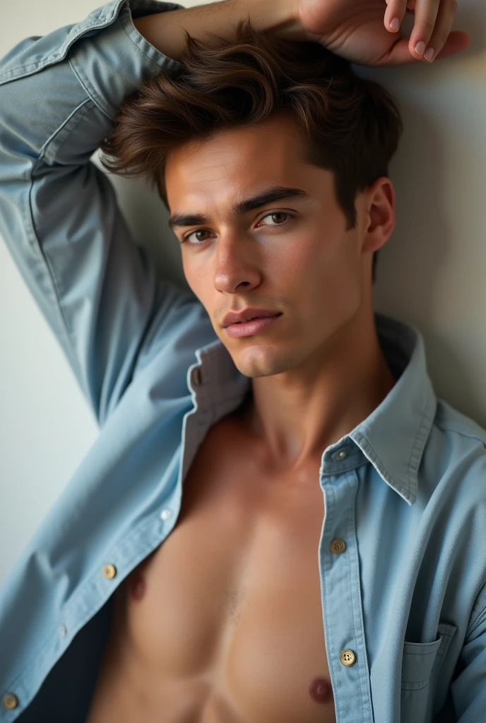 Has a water that has the shirt unbuttoned in his photograph, He has one arm resting on his head and his face is slightly looking at the camera in this photograph.