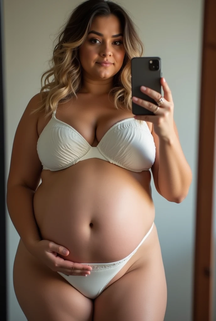 Beautiful curvy milf woman with brunette blonde dyed hair and quince belly, wearing a white padded bra, is holding her belly and taking a selfie with the phone in the mirror