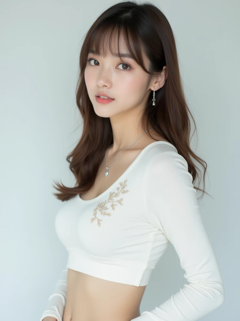 a portrait-style photograph featuring a gorgeous Asian woman with light skin and straight, shoulder-length brown hair with bangs. She is wearing a white, long-sleeved top with a cropped design, revealing a small portion of her midriff. The top has subtle embroidered details on the left side. She accessorizes with a delicate necklace featuring a small pendant and matching earrings. The background is plain and light-colored, which keeps the focus on the subject. Her expression is neutral, and she is looking directly at the camera.