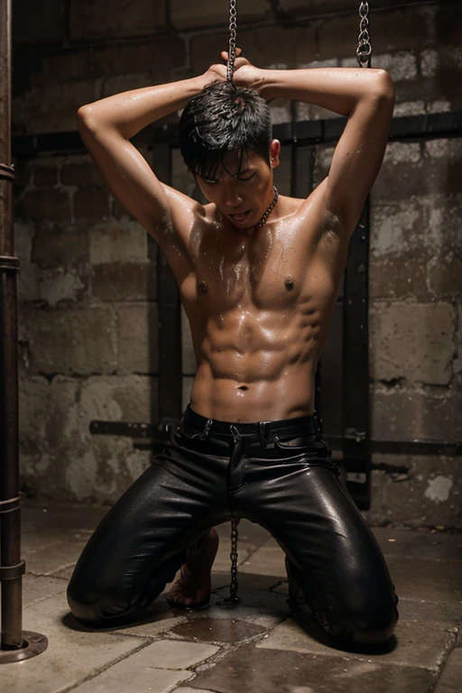 A shirtless skinny asian young man in wet leather pants screams while chained to a metal frame in dungeon