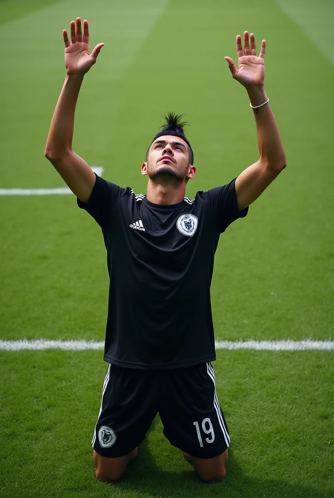 A young man with a mohawk kneeling with his hands raised to the sky on a soccer field wearing a black shirt with the number 19.