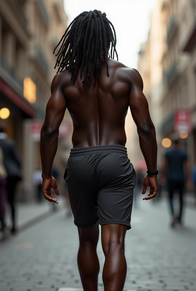 A darkskin man with long dreads, walking down a sidewalk. He has a very fit, round, and bubbly pair of buttocks. He is wearing fitted shorts that emphasize the voluptuous shape he owns. The perspective is from directly behind him.