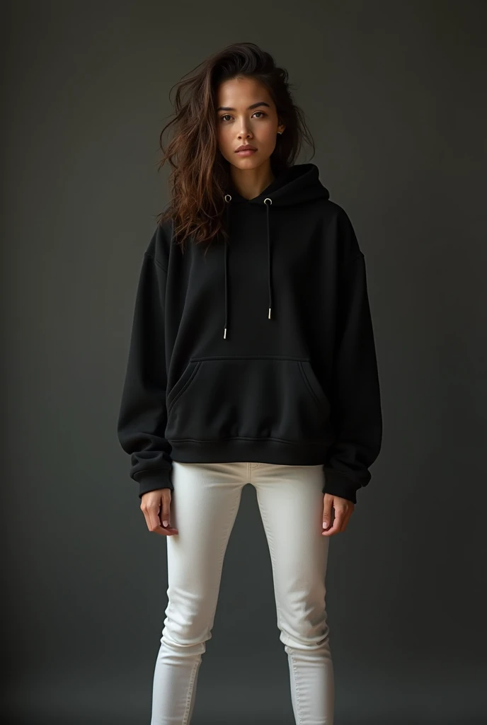 Une jeune femme se tient debout, sûre d'elle, légèrement penchée en avant, le regard intense. Elle porte un hoodie noir surdimensionné, révélant son ventre. Ses mains sont dans ses poches et ses cheveux sont volumineux et légèrement désordonnés. L'arrière-plan est sombre et neutre, ce qui met en valeur sa pose et son expression puissantes. Elle porte un jean blanc et elle écarte les jambes de 50 cm.