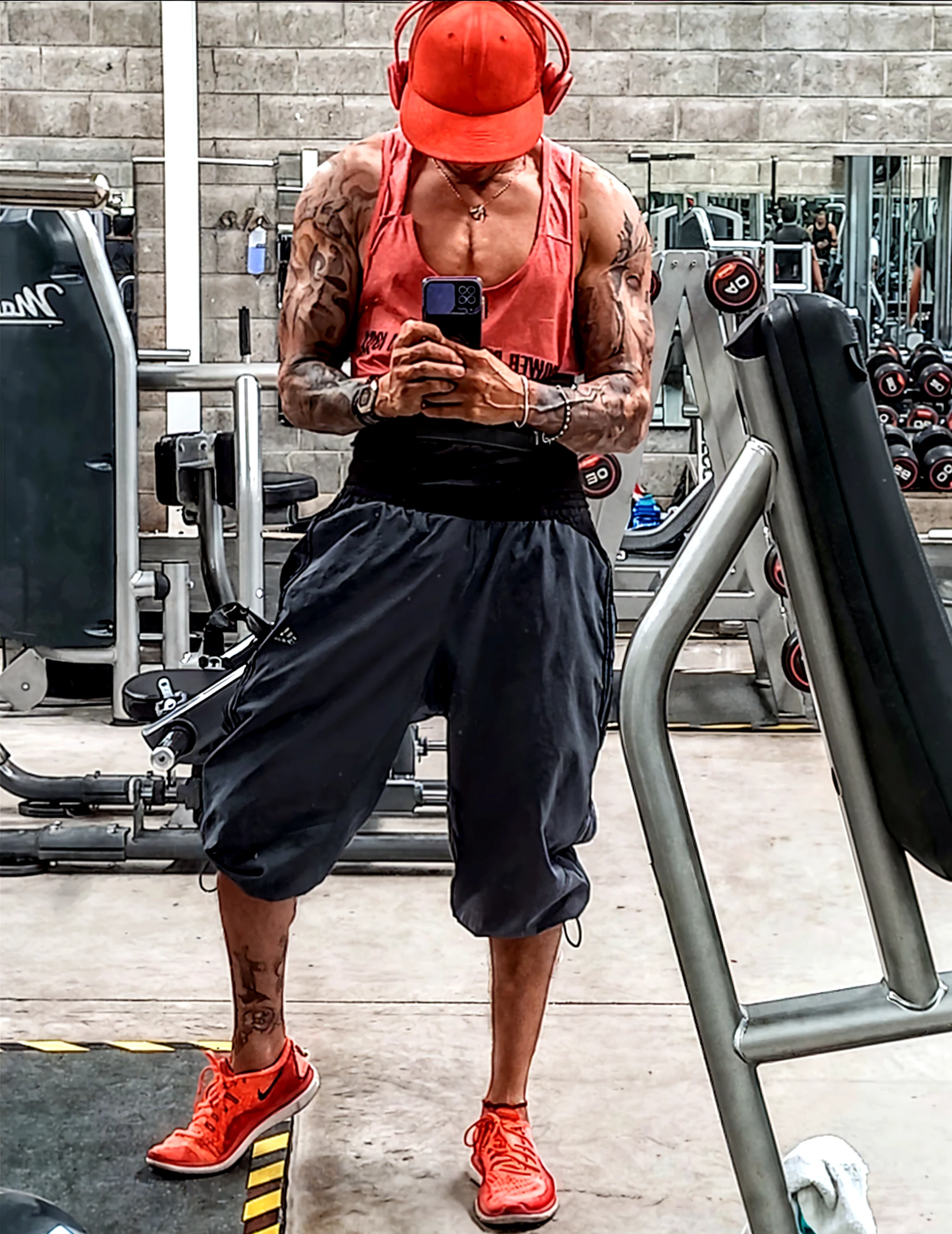 Strong, muscular mixed race gas station attendant sitting on bathroom floor in navy blue underwear, red cap and discreet gold chain around the neck, Looking at cell phone, Being watched by a man sitting on the bench.