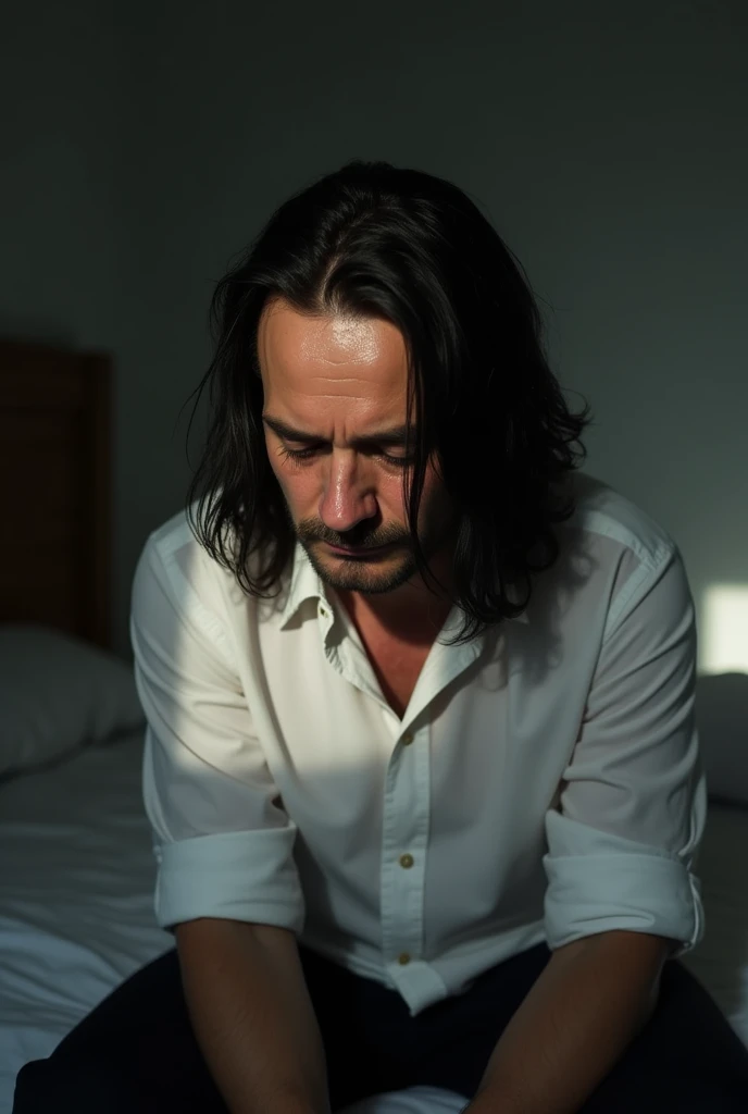 A sad man with pale skin is crying. He is sitting on the bed wearing a white shirt. He has long black hair and black eyes. He has a bit of a beard. He is middle-aged and has an innocent appearance. He is crying and has bags under his eyes