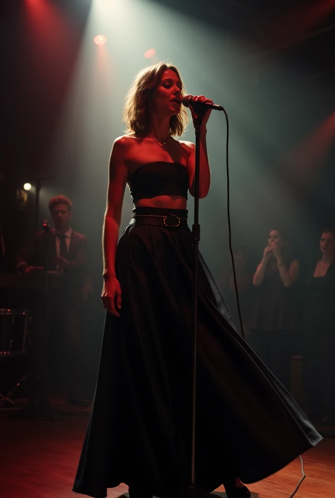 Photo of a singer on a small stage. Instead of a top, she wears a belt, she covers her chest. she wears a black skirt. She sings into a microphone.