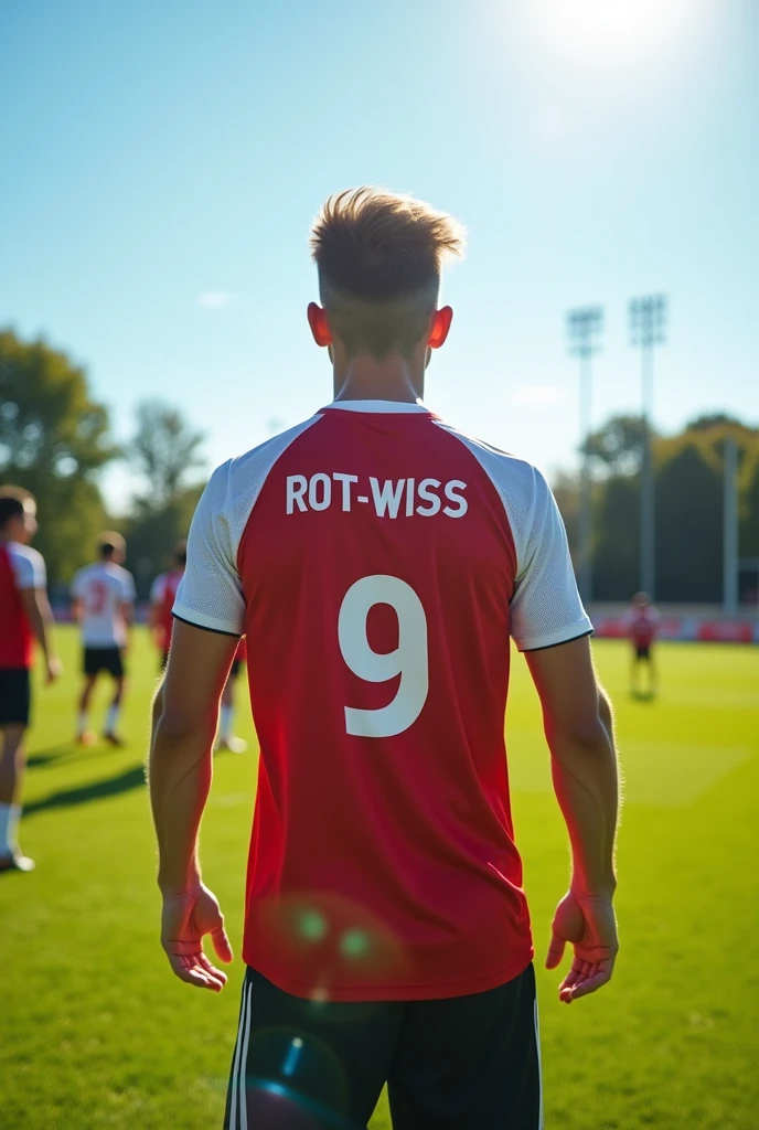A 17 year old football player training at a training camp ,Wearing a white and red jersey,Number 9, The jersey says Rot-Weiss Essen , photographed from behind