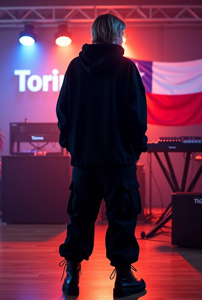 a trap singer, male, dark blond, looked from back, wearing all black clothes, oversized, hoodie, wide trousers, boots, chains, streetwear, standing on a music studio, con la bandera de chile, y la palabra "torino" en alguna parte