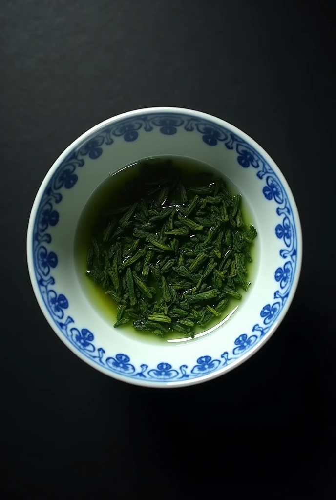 The camera looks down from directly above on a Chinese blue and white porcelain teacup filled with dark green one-core and two-leaf Chinese mountain tea.，((Right beneath the surface, You can see that after drying, the Chinese high mountain dry tea with one core and two leaves is soaked in dark green.)),simple，Movie Lighting，专业photography，Studio Lighting，Black desktop background，photography，Intricate details，Ultra Detail，Hyper-photorealism，8K Ultra HD （（Top-down view，Top view, bird's eye view））