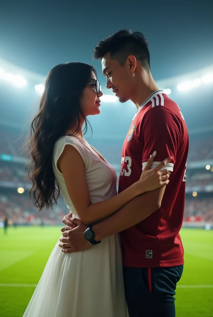 A man and woman in standing looking at each other with love and hugging each other . woman has black hair and wearing a white dress and glasses.boy is wearing 32 number sport jersey.man is taller than girl they are standing in football ground