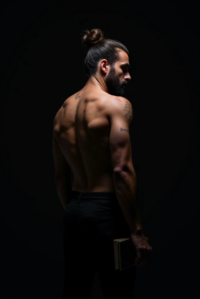 A man is seen from behind. He is turning slightly back. He is looking to the right. His hair is tied in a bun and he has a short beard. His upper body is exposed. The man is wearing dark pants. In his left hand, he is holding something indistinct, possibly a book or notebook. The background is completely black, which makes the details of the body stand out clearly.