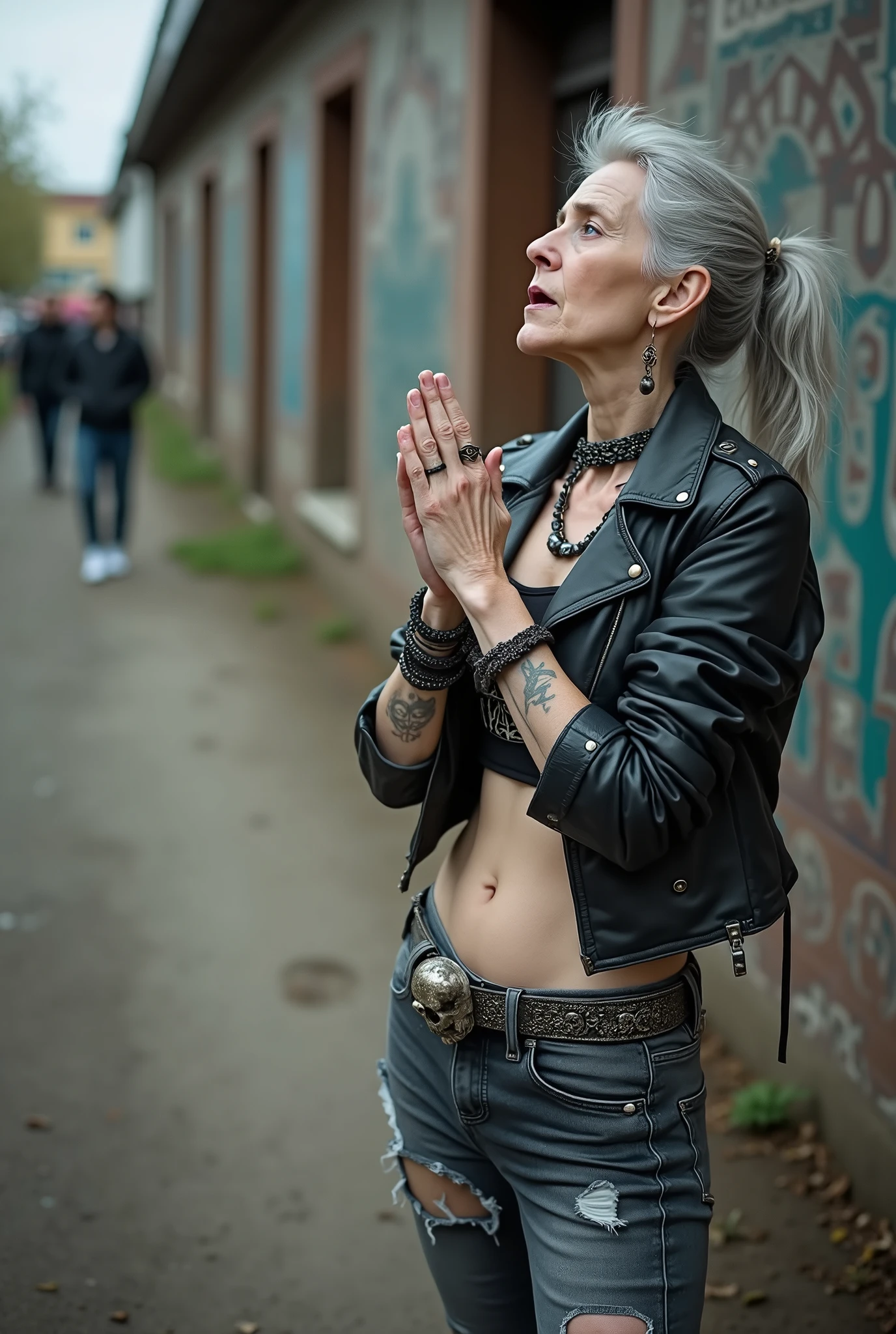 russian old milf woman, biker gang member, long grey hair (bump, quiff and ponytail) with very light blue eyes, extremely pale. Thin. Sad, humble face. Wearing cropped black moto jacket with side zippers, black cropped tank top with pentacle logo, skinny black jeans with holes and white tennis sneakers. Lots of metallic bracelets. Tacky wide belt with massive skull and bones buckle . Both hands in prayer. Demonic tattoos. Lots of rings. Long earrings. Looks up with amazement because she thinks God is talking to her, mouth and eyes open. Skinny legs, narrow hips. People around look at her