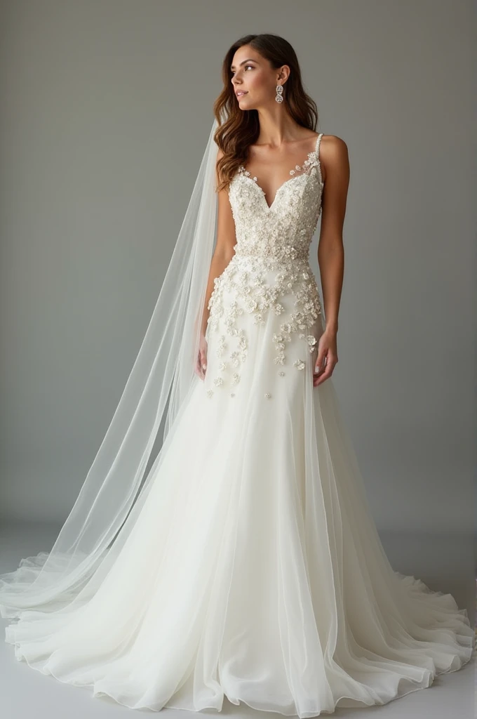 Your perfect wedding dress is an elegant A-line model with a straight neckline that highlights the bust in a classic way.. The bust is adorned with sophisticated floral and glitter applications., giving a touch of glamour and delicacy. The tulle skirt flares gently to the floor, flowing with lightness and grace, and also features applications that add a subtle and refined charm. The waist is marked, enhancing the silhouette and creating an elegant shape. The dress is completed by a long tulle veil, decorated with the same floral applications and sparkles, that complement and harmonize with the rest of the outfit, creating a stunning and charming look.