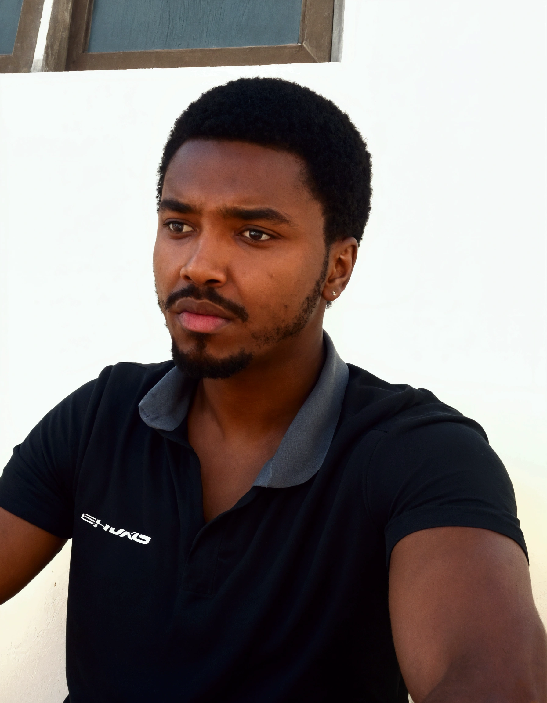 a bearded man sitting in front of a white wall with a cell phone, looking intensely at the camera, 23 year old. black jersey.