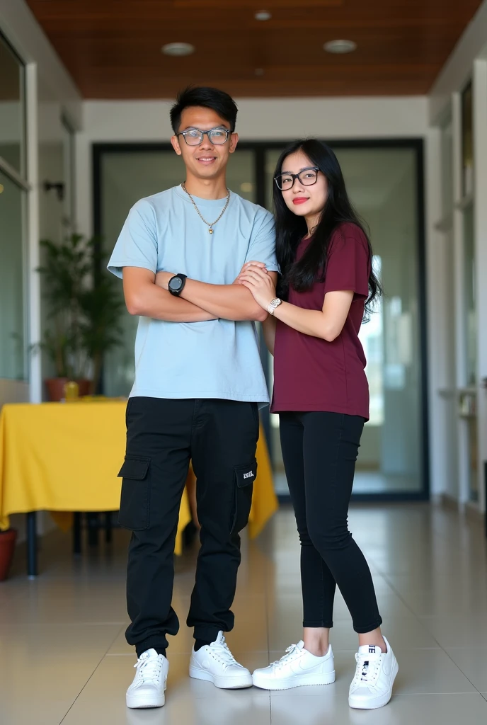 Image is a vertical, full-body photograph of two Filipino people standing indoors. The person on the left is a young man with short black hair, wearing glasses, a light blue shirt, black cargo pants, a watch on his left wrist, and white samba shoes. He has a light skin tone and is smiling no teeth with his arms crossed. The person on the right is a young woman with long black hair, wearing glasses, a maroon t-shirt, black skinny jeans, and white nike airforce shoes. She has a lighter skin tone and is slightly smiling while touching the man's arm. The background features a modern interior with a wooden ceiling, glass doors, and a yellow tablecloth on a table to the left.