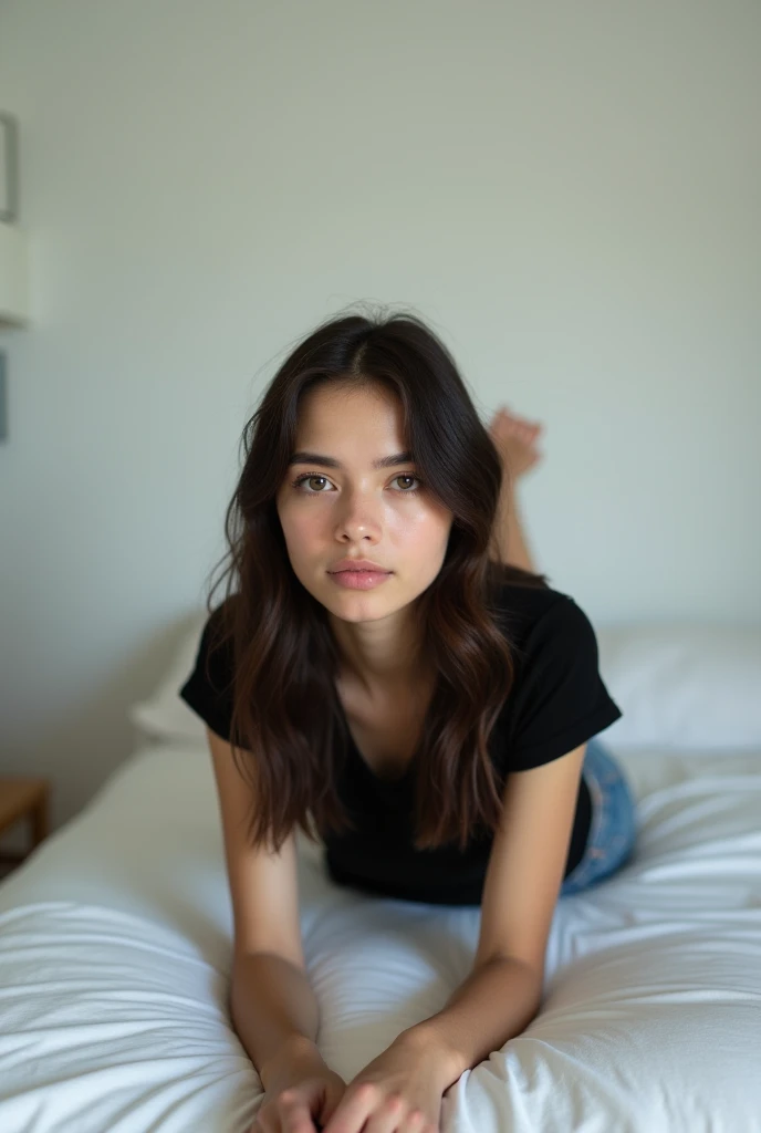 brunette, smile, flat chest, skinny face, white wall, no decoration, jean shorts, black t-shirt, lying on stomach on bed, looking at camera, photo from behind